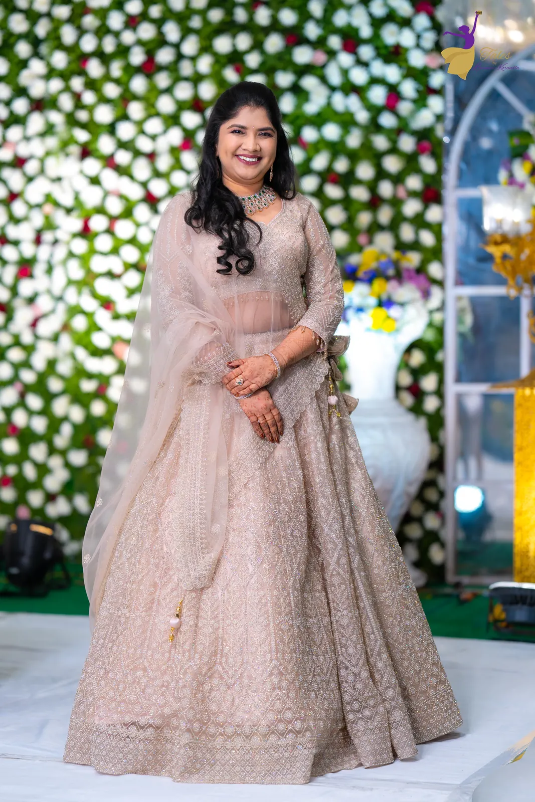 Full-length bridal portrait of Priyanka in a blush lehenga against white flowers