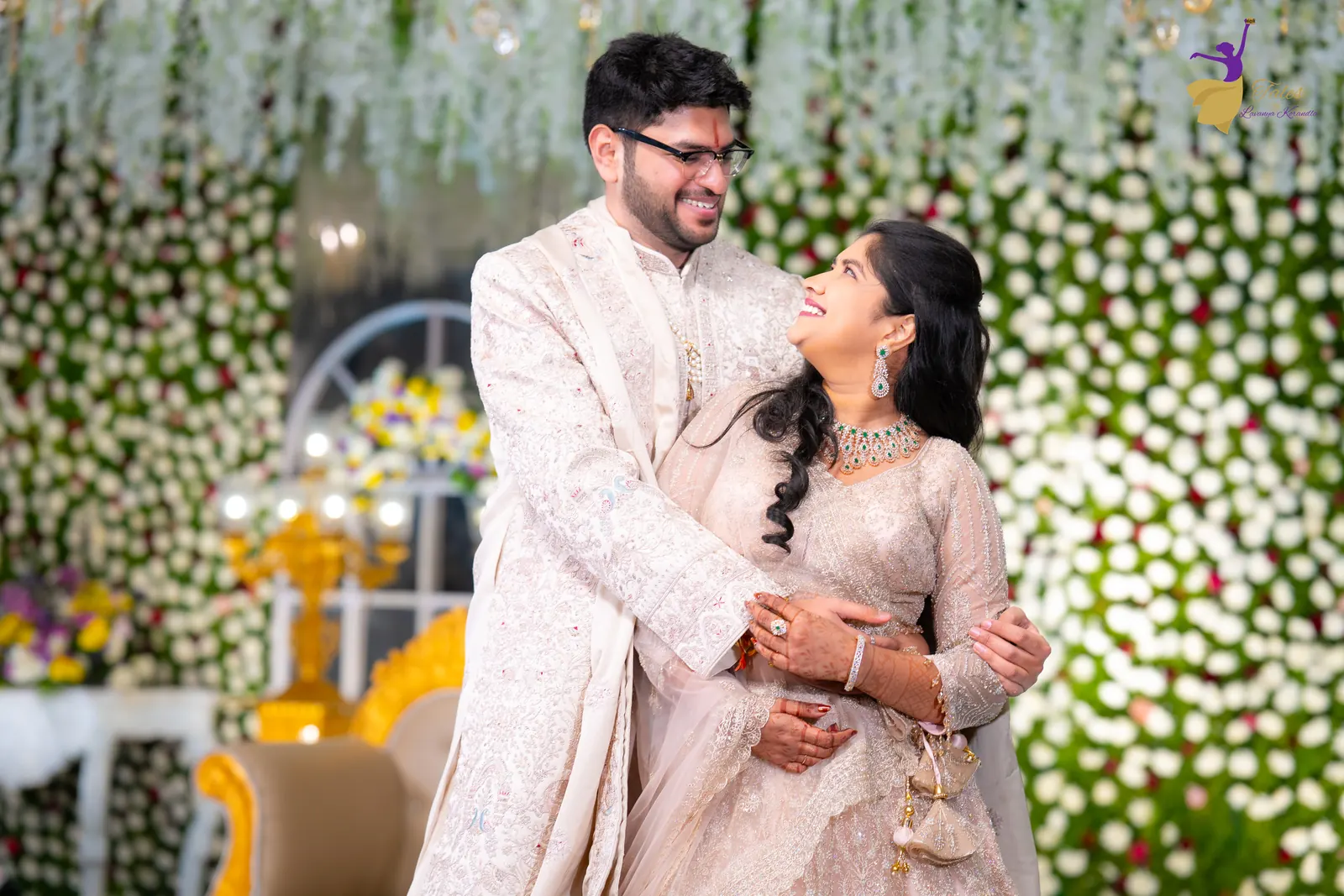 Aditya holding Priyanka close against a white floral wall at their Hyderabad reception