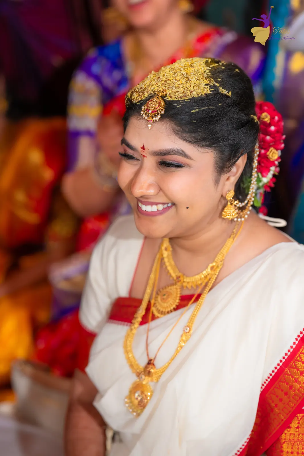 Bridal portrait of Priyanka in a white and red silk saree with bashikam, smiling