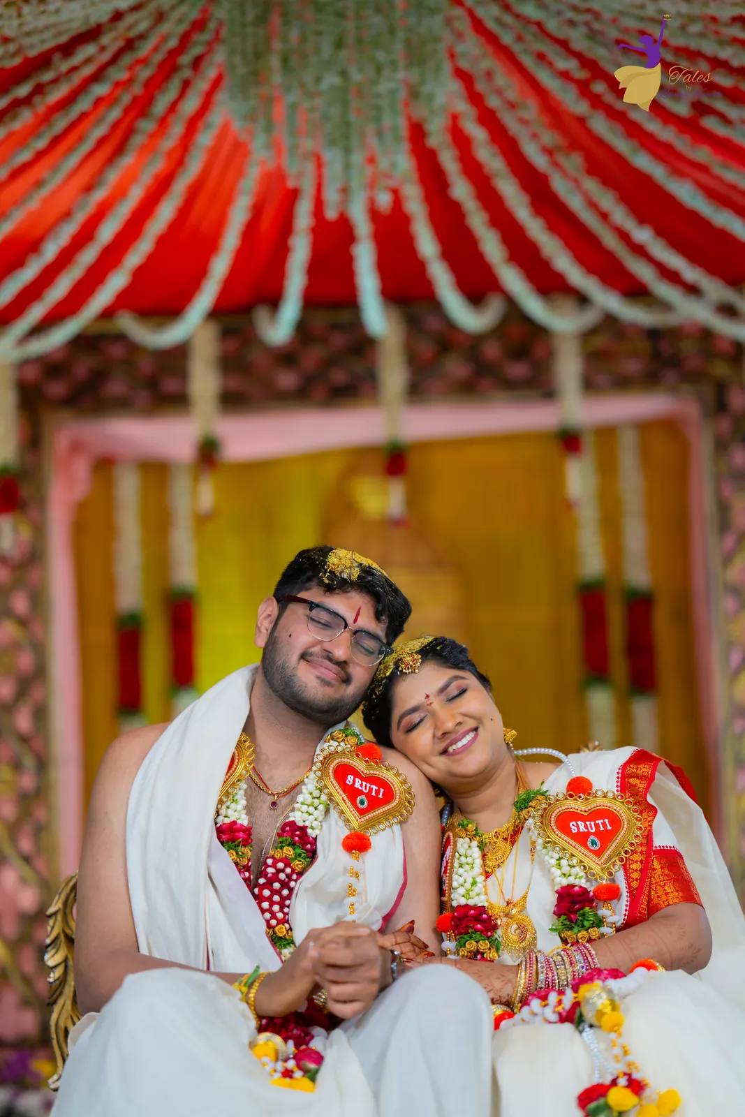 Aditya and Priyanka smiling, heads together, under the red-and-white mandap canopy