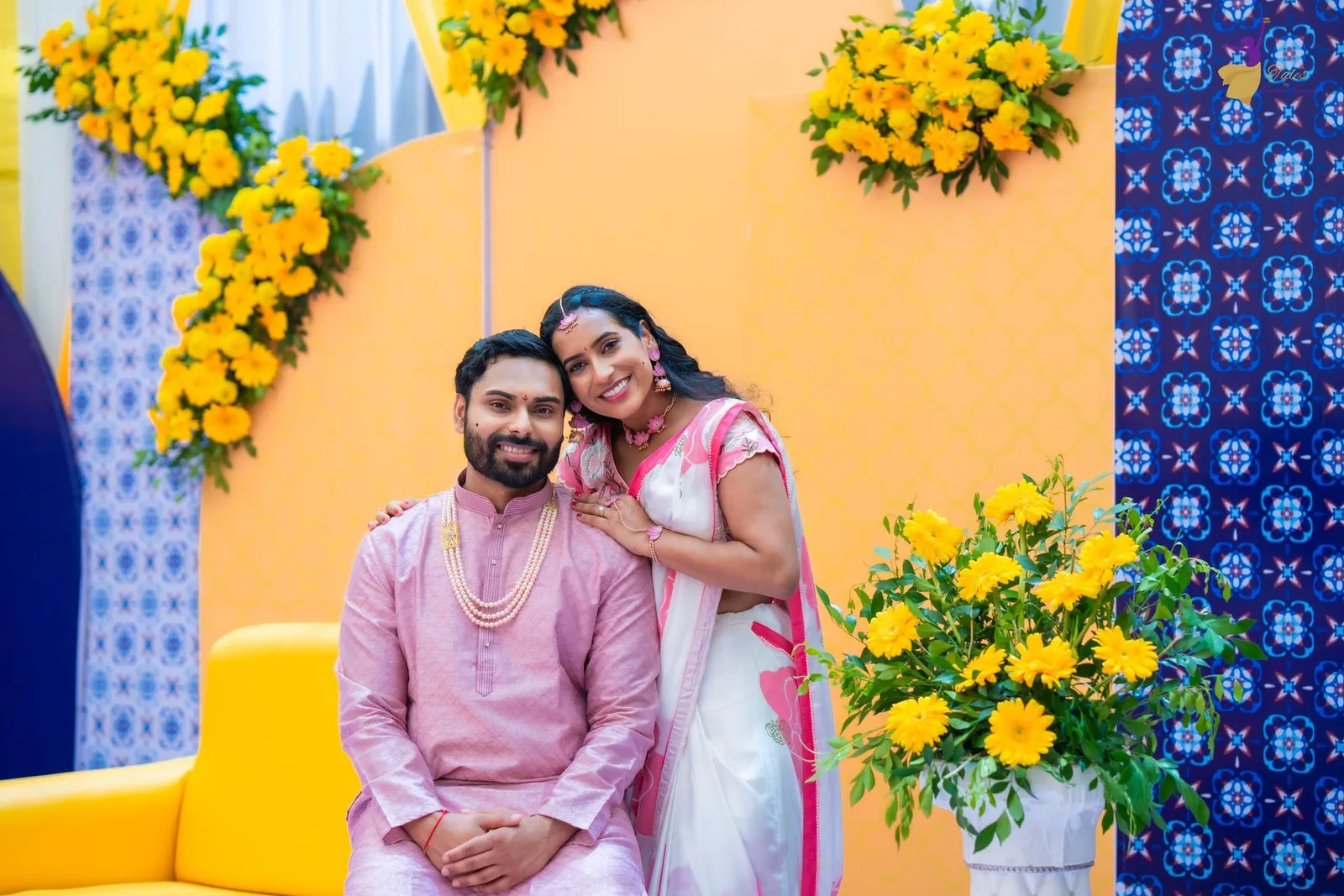 Manoj and Priya smiling on a yellow sofa at their Haldi