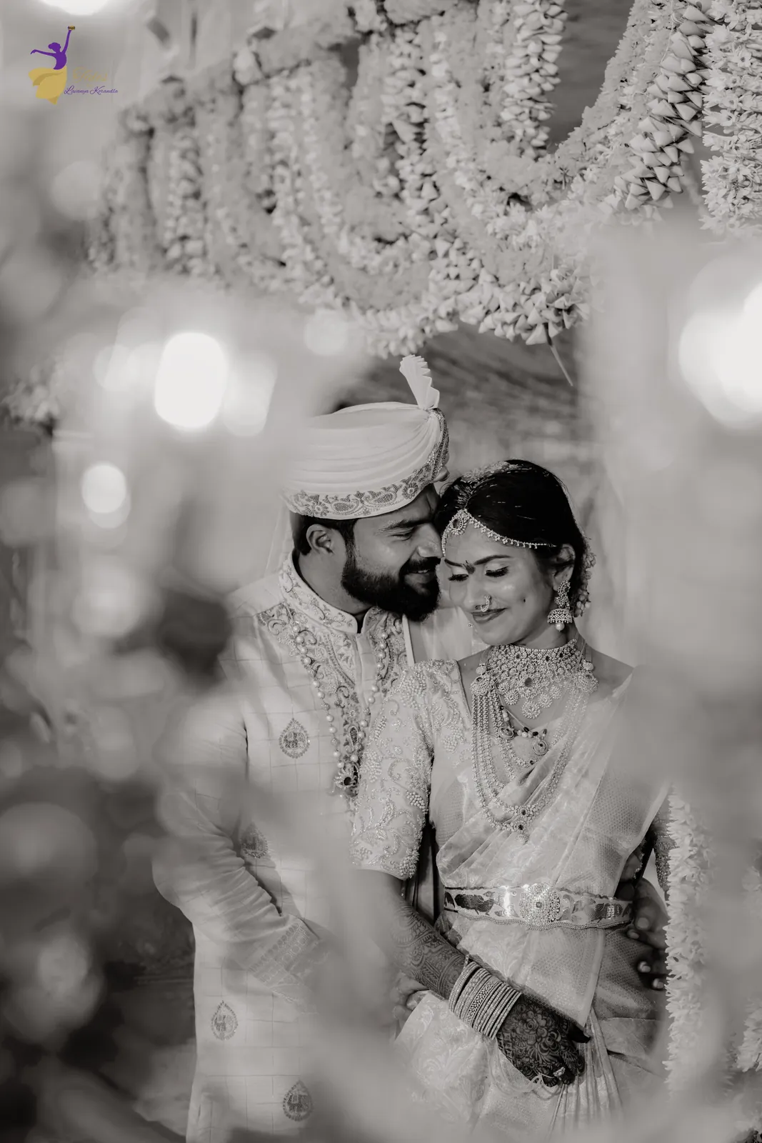 Black-and-white portrait of the bride and groom under hanging floral garlands, wedding day