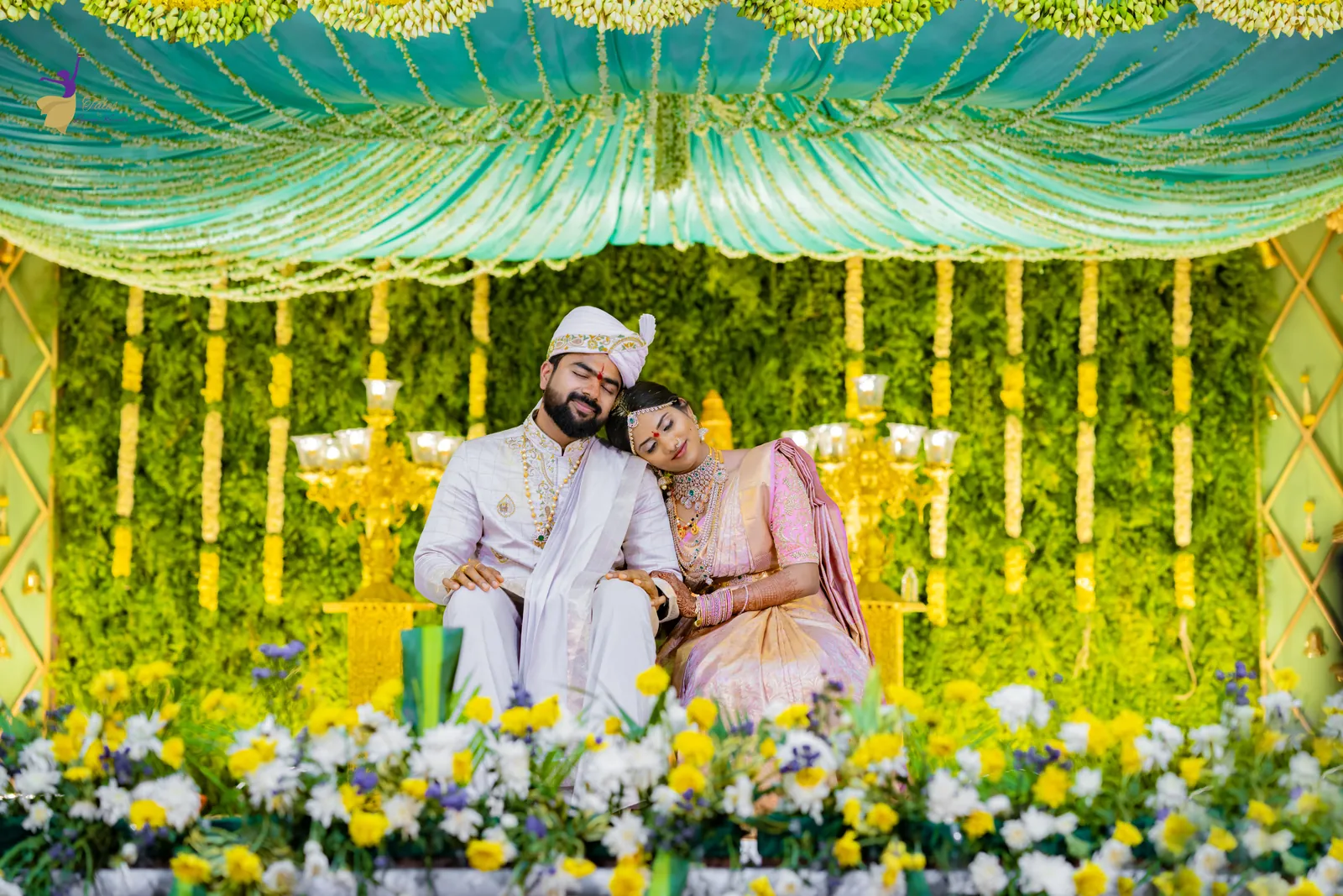 Krishna and Vishwasa seated together on a green and gold floral wedding mandap