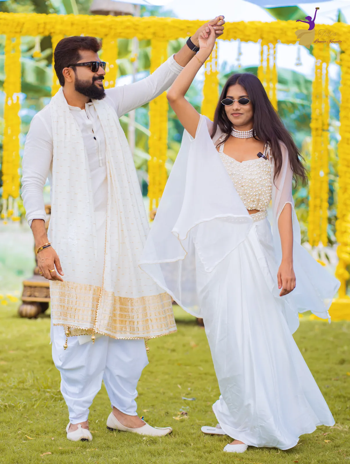 The couple in white twirling on the lawn in front of marigold strings at the haldi