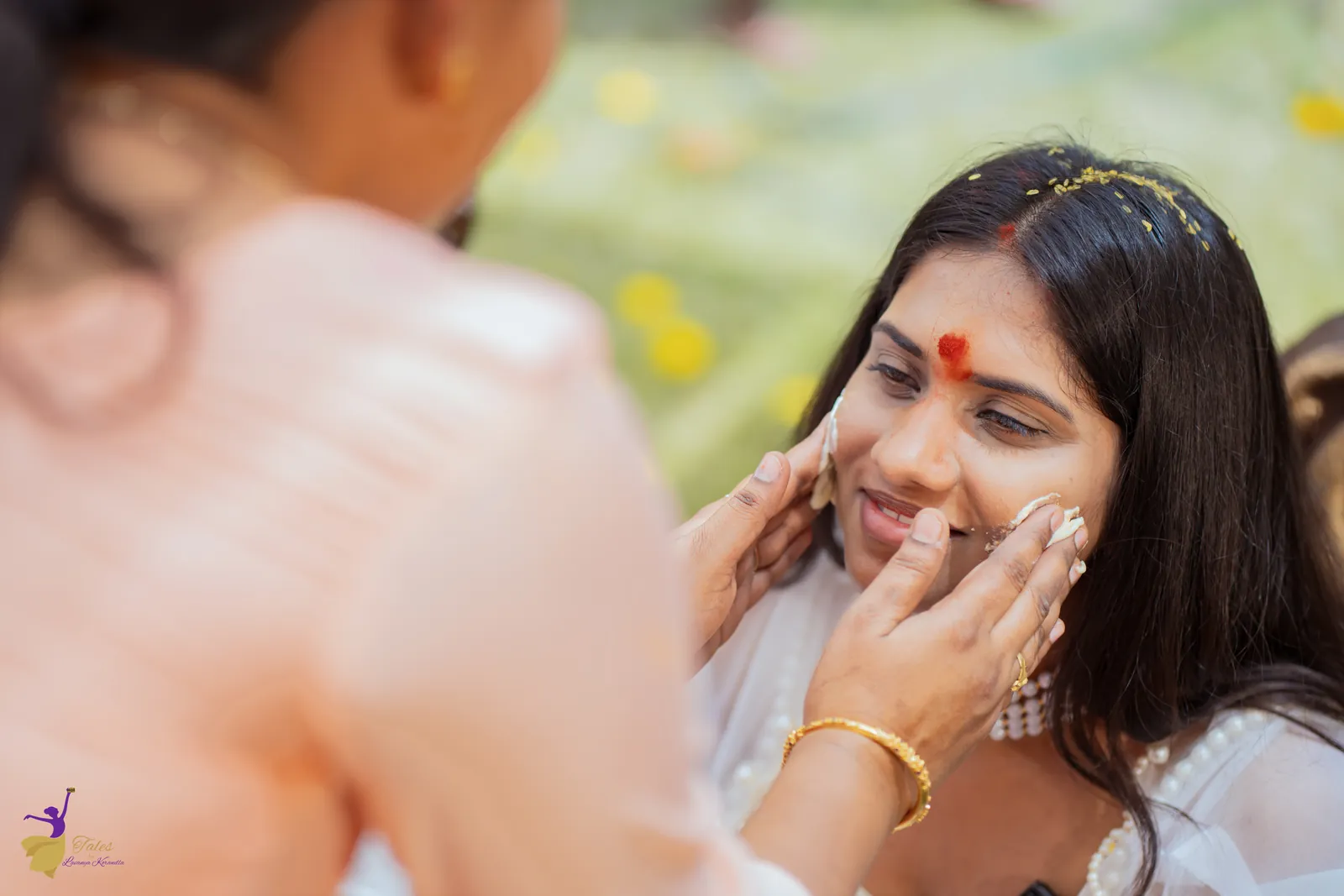 Turmeric being applied to the smiling bride’s cheeks at the haldi