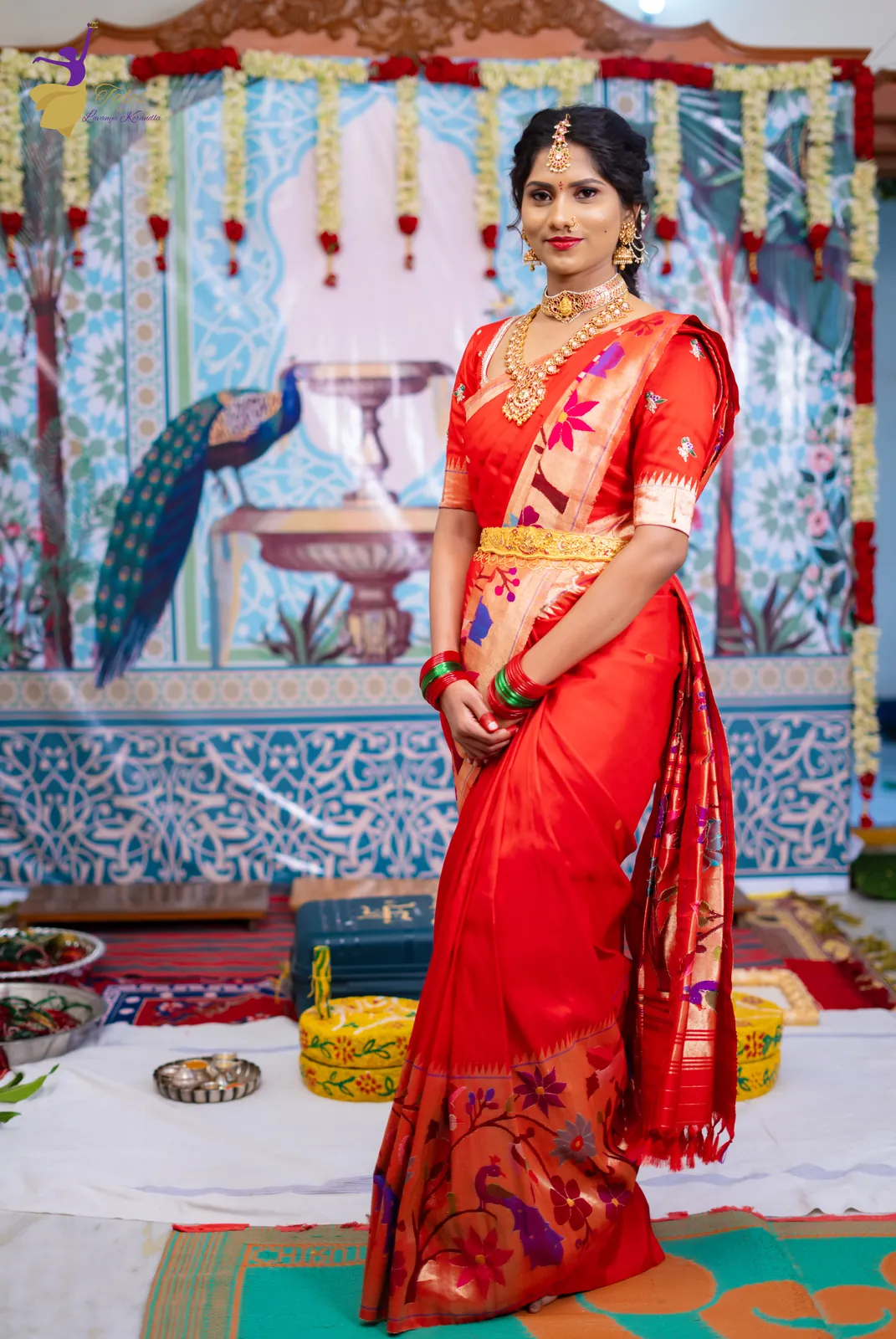 Vishwasa in a red silk saree before a peacock and fountain backdrop at her Pellikuthuru