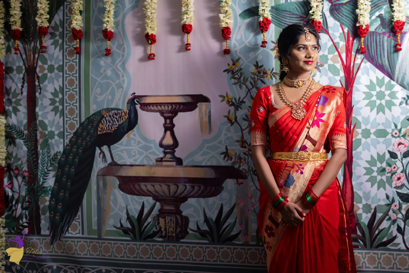 Vishwasa in red silk standing beside the peacock fountain decor at her Pellikuthuru