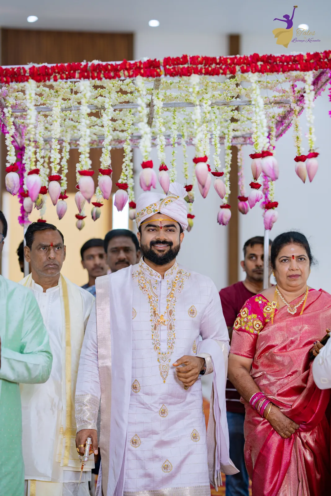 The groom’s entry under a pink and white floral canopy carried by family