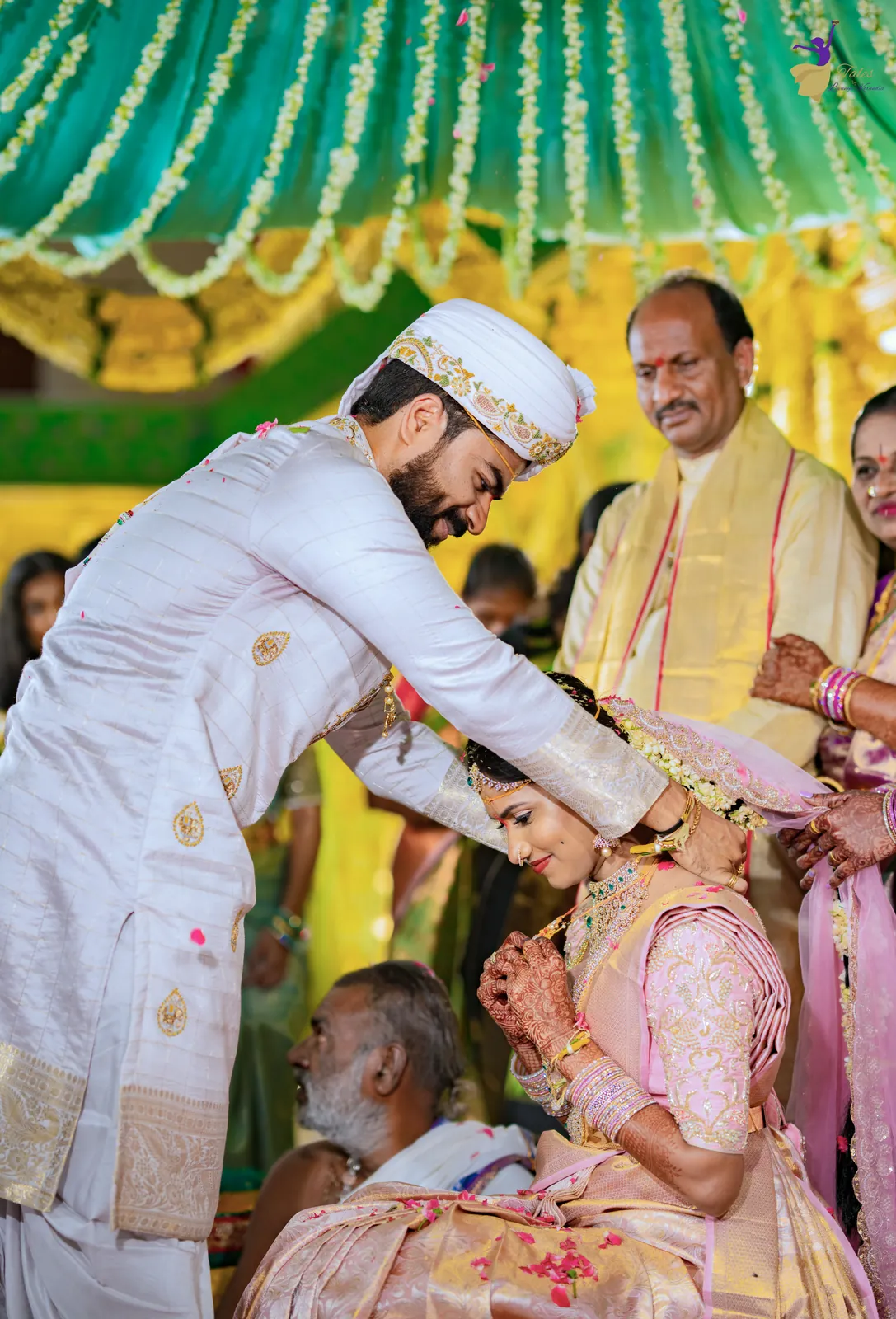 The groom tying the thali (mangalsutra) for the bride under the green and gold mandap canopy