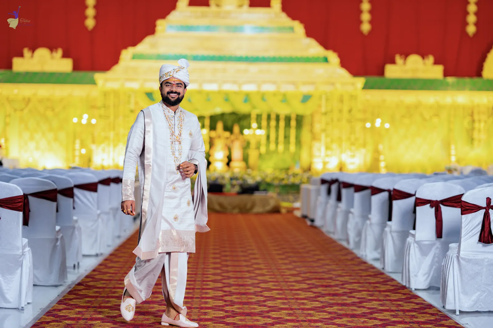 Wide shot of the groom walking down the red carpet towards the golden mandap stage