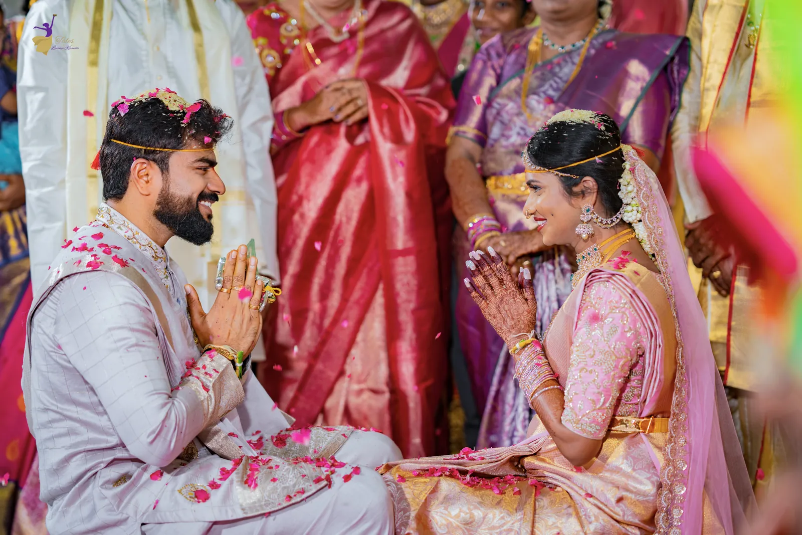 The bride and groom with folded hands during the rituals, guests in silk sarees behind them