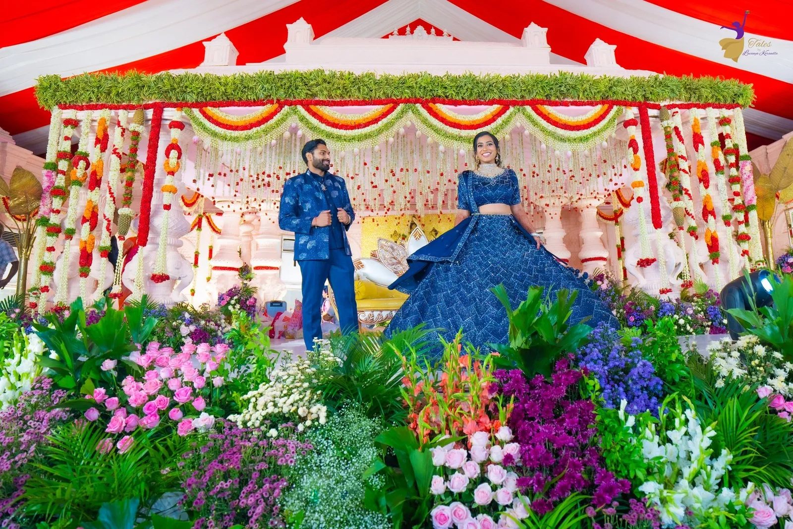 Manoj and Priya in midnight blue on a flower-filled pre-reception stage, Amalapuram wedding reception photography – TBLK