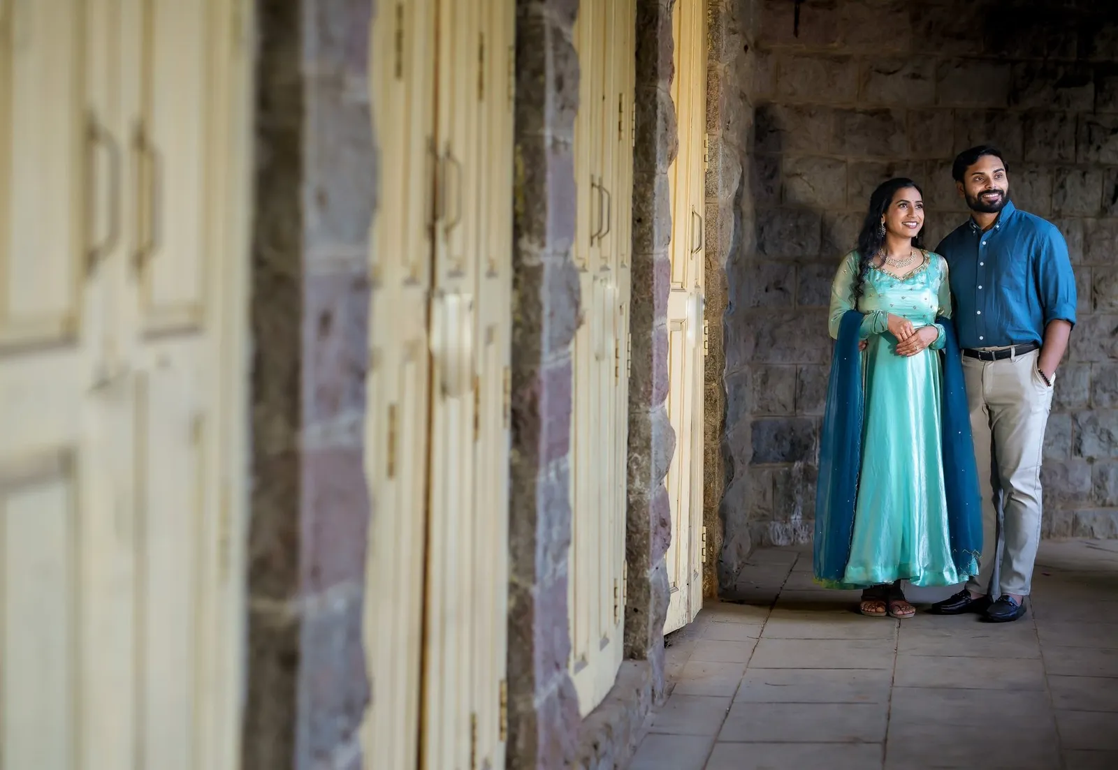 Manoj and Priya standing by an old stone corridor and wooden doors, old-city Hyderabad pre-wedding shoot – TBLK