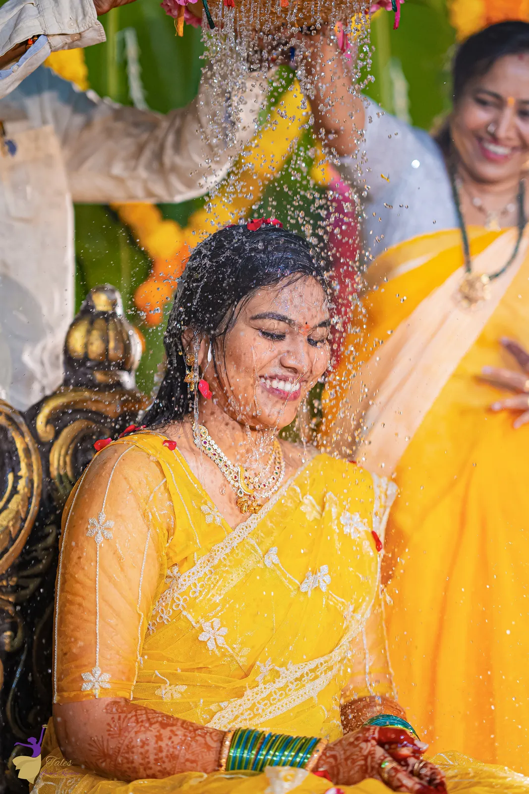 Family pouring blessings of water and turmeric over a smiling Anuhya at the haldi