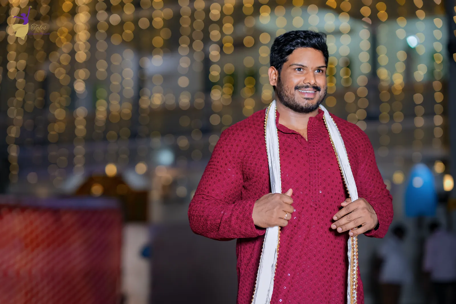 Ravinder in a maroon kurta and white stole smiling under a curtain of fairy lights at his mehendi night