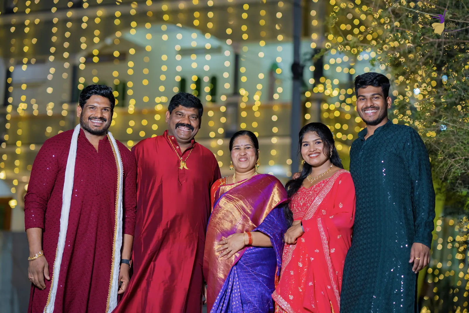 Wide shot of Ravinder with his family and cousins before a glittering wall of fairy lights at the mehendi