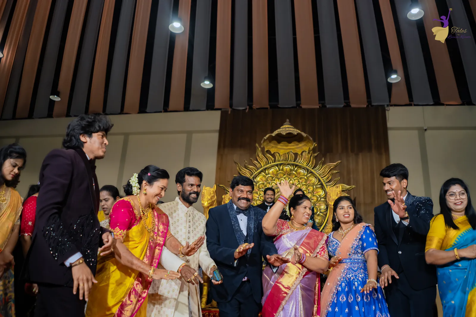 Wide shot of the reception stage crowded with family and friends under a wooden-slat ceiling