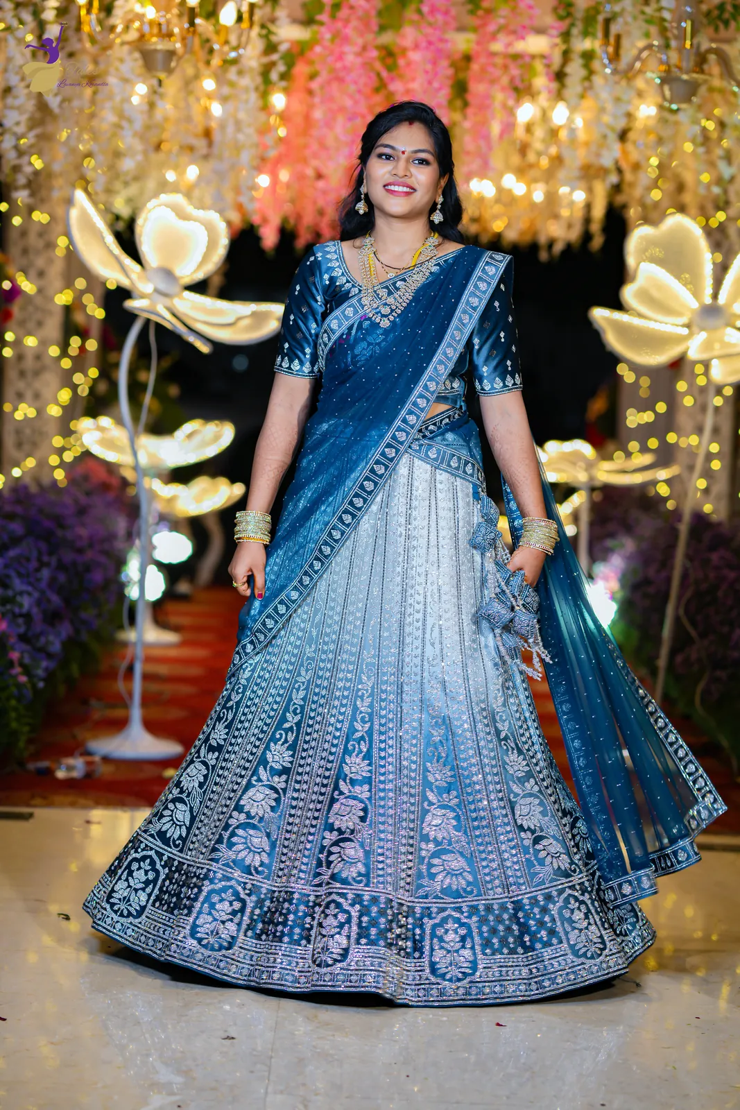 Bridal portrait of Anuhya twirling in a blue and silver lehenga under hanging florals