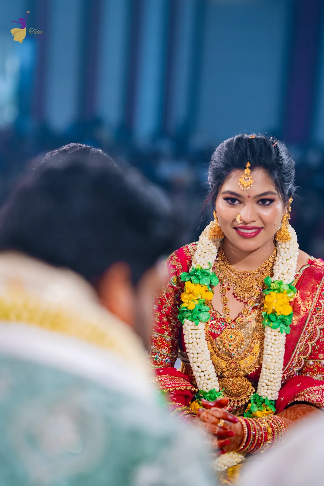 Anuhya smiling at the mandap in jasmine and marigold garlands, a soft emotional moment