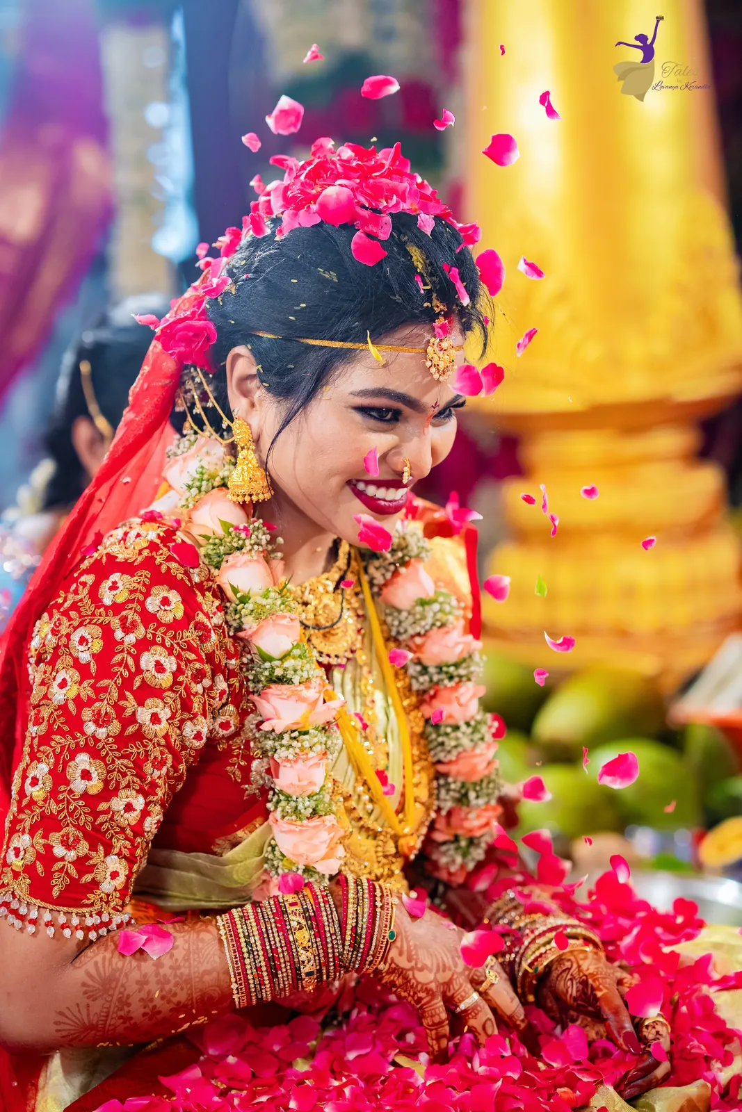 Anuhya in red and gold smiling as flower petals shower over her