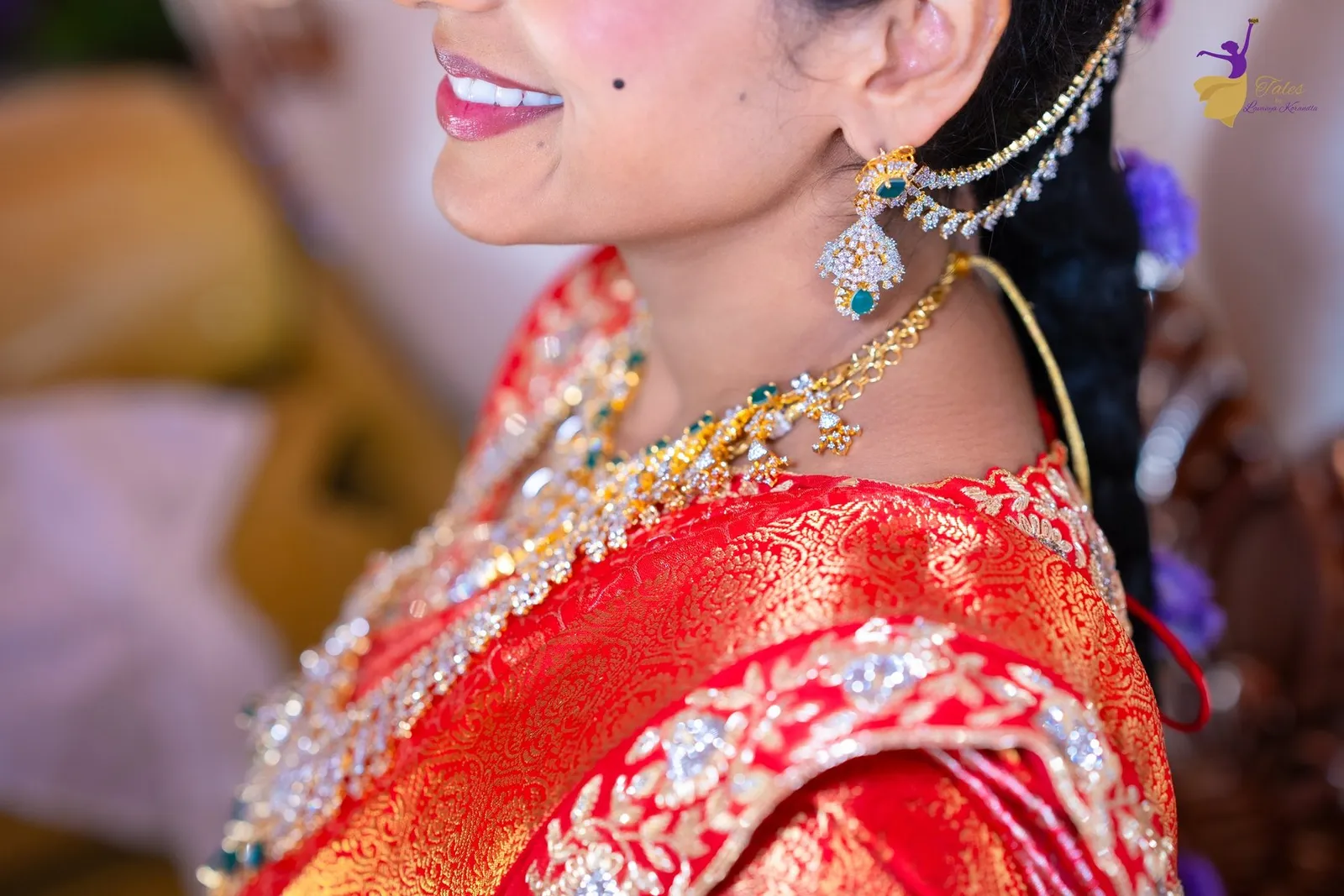 Priya smiling in profile in a red silk saree and gold jewellery