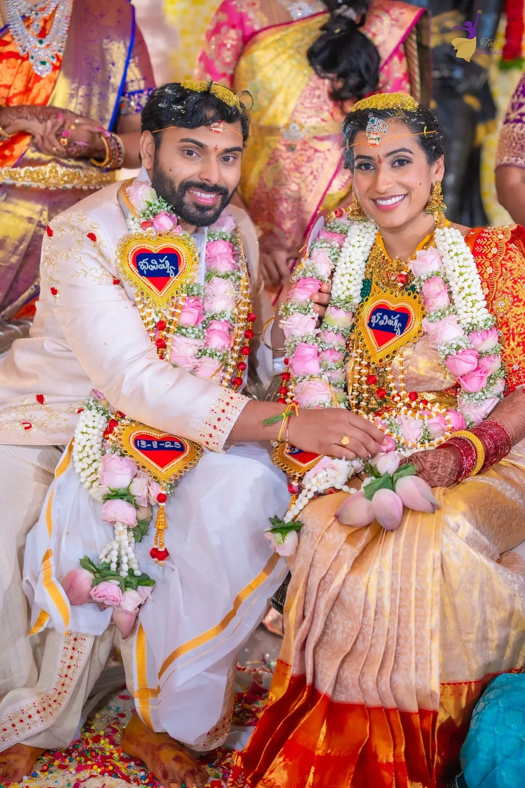 Manoj and Priya seated in rose garlands with lotus buds, smiling on their Telugu wedding day in Amalapuram – TBLK