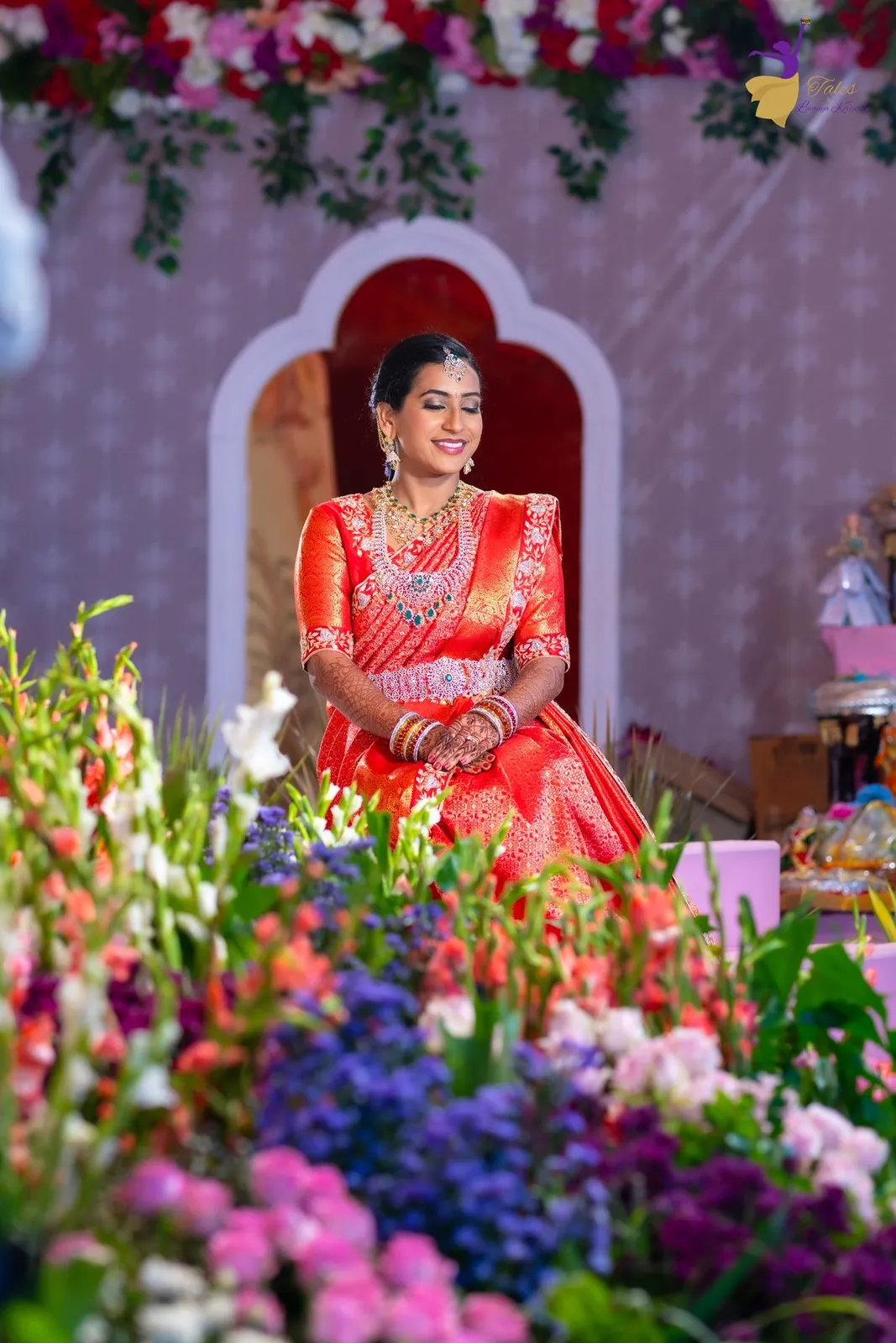 Priya behind purple and pink flowers under a decorative arch, wedding day