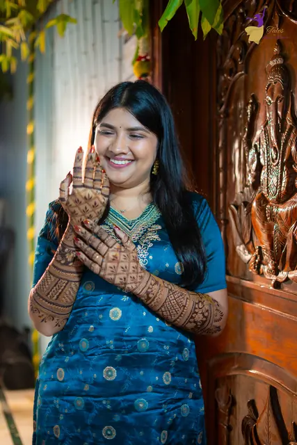 Priyanka smiling with her henna hands raised by a carved wooden doorway