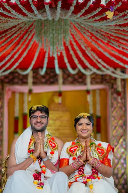 Aditya and Priyanka with folded hands under the red-and-white mandap canopy