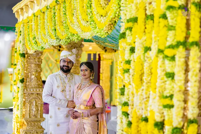 The bride and groom standing close between towering yellow and white flower pillars
