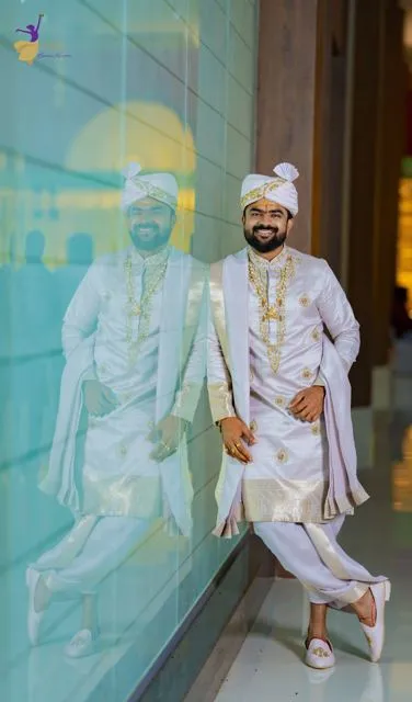Groom in white traditional wear leaning by a glass wall