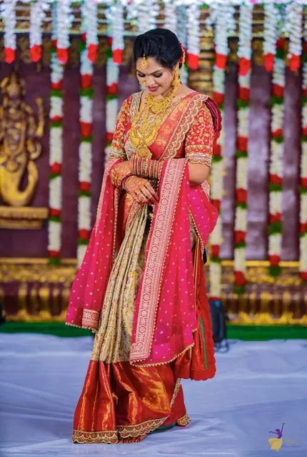Bride in pink and gold silk saree on a flower-garlanded stage