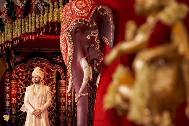 Groom in a temple-like setting with red pillars and gold idols