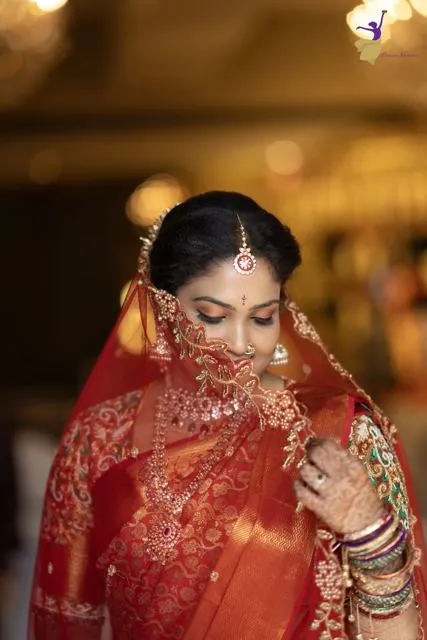 Bride looking down in a deep red saree with sheer gold-motif veil