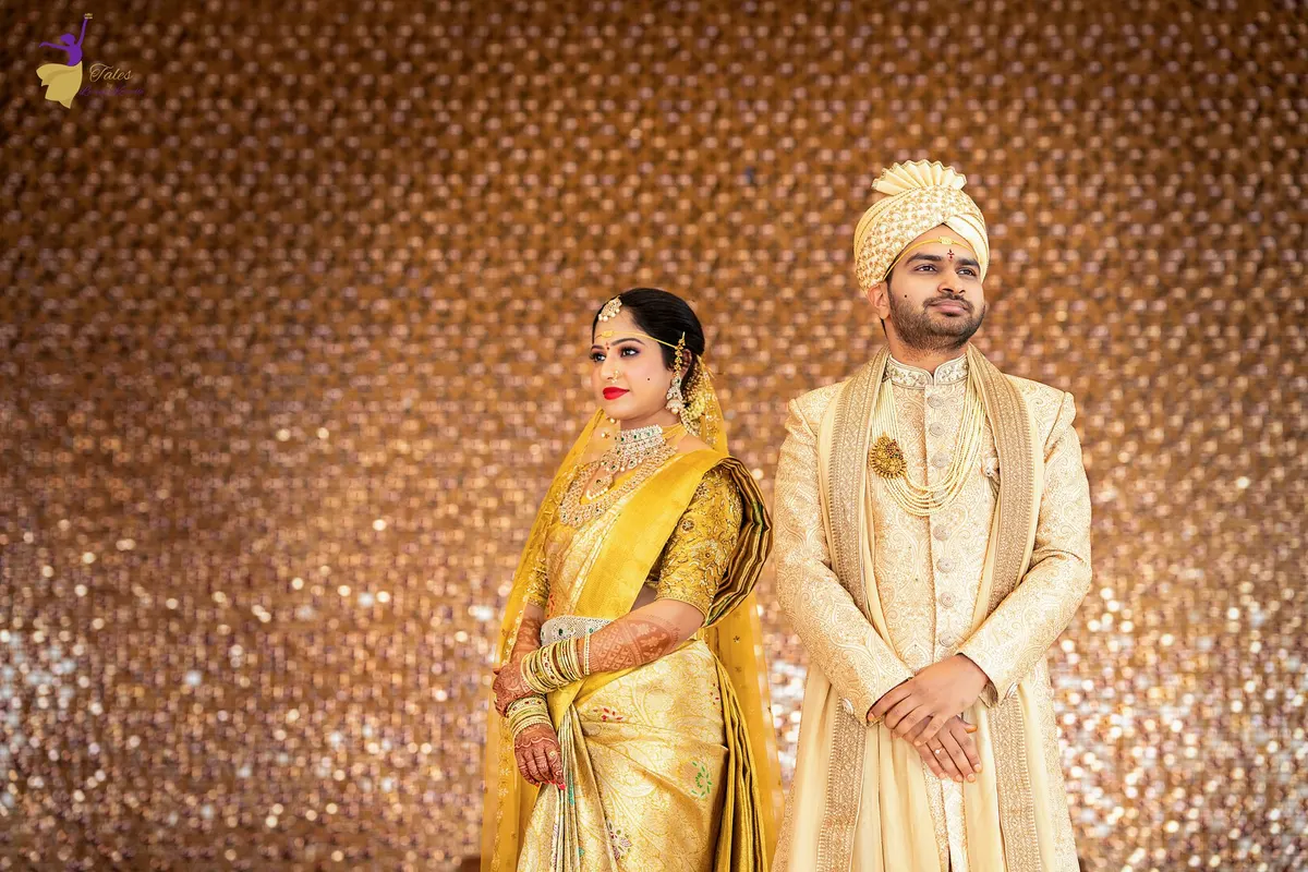 Wedding couple in gold and cream attire against a shimmering bronze backdrop, Hyderabad