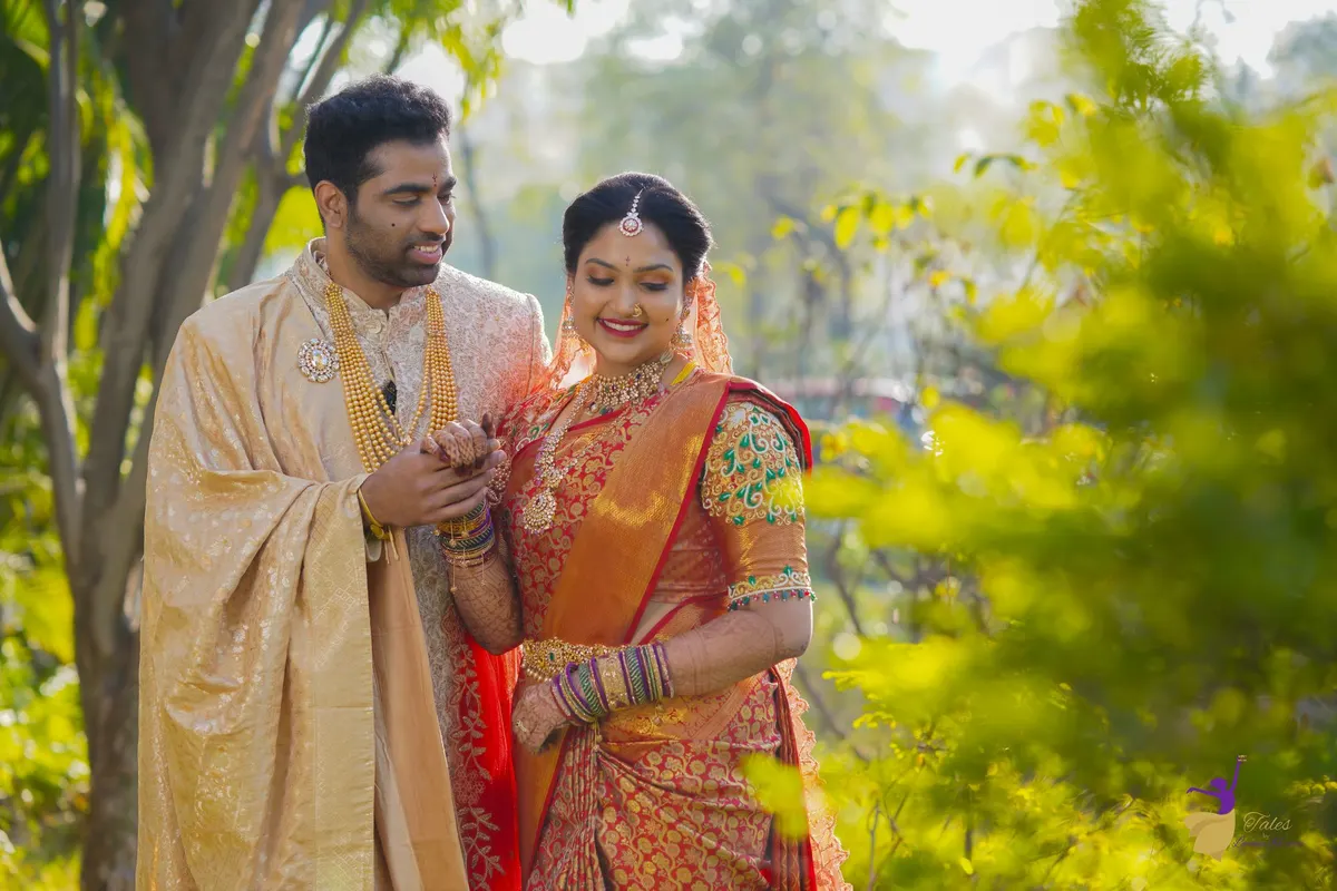 Bride in red silk saree and groom walking through a sunlit garden, Hyderabad wedding
